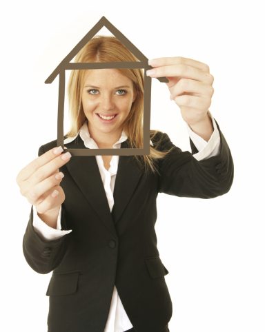 Business-Foto einer Frau im Anzug, die lächelnd einen Hausrahmen aus Holz hält