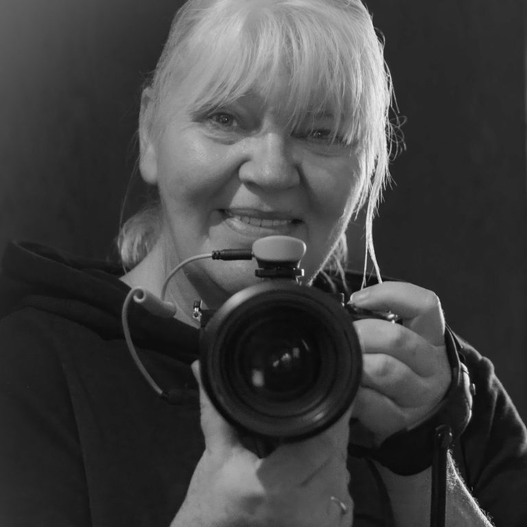 Dolly Niass, mobile Fotografin von madXgrafie, hält eine Kamera in einem schwarz-weißen Porträt.