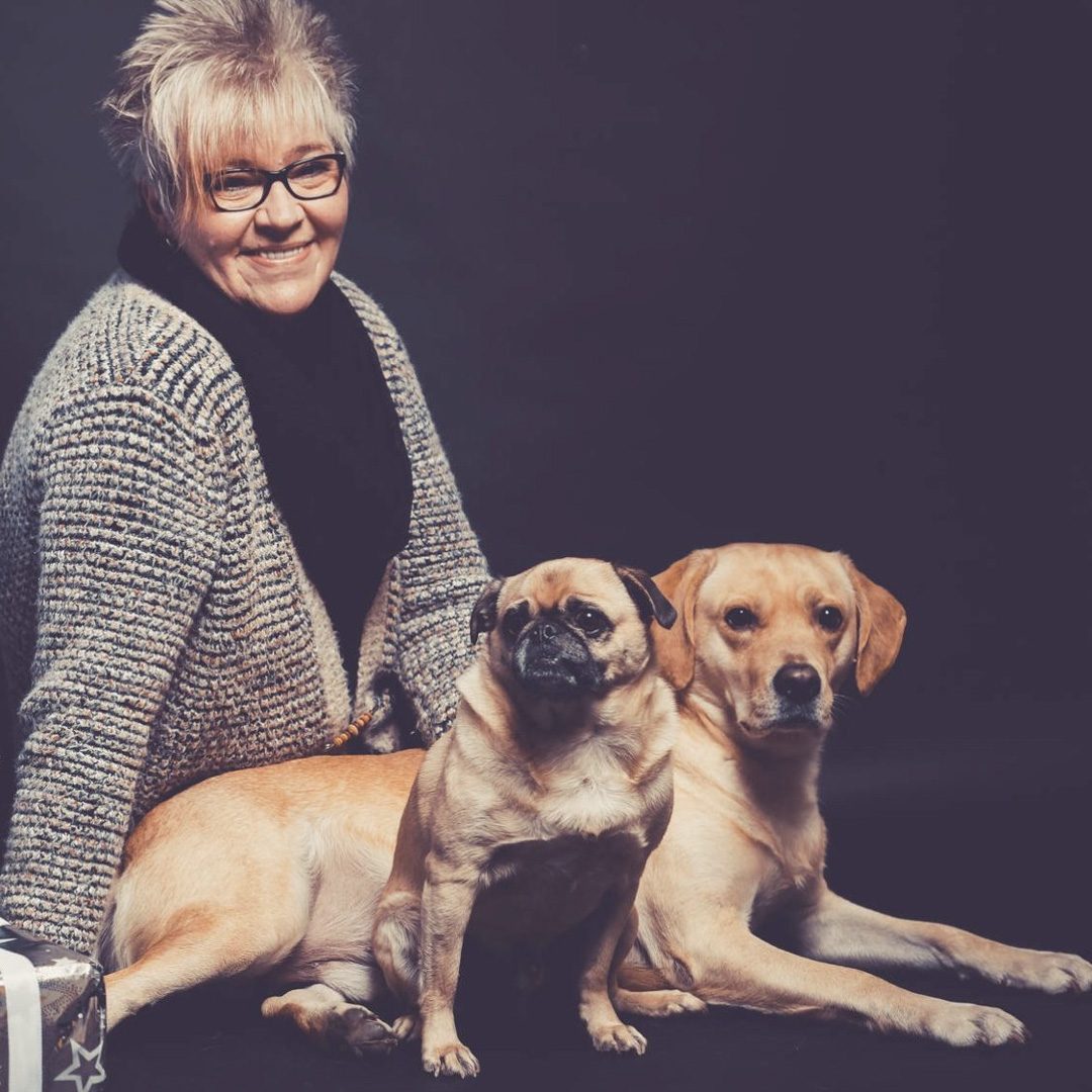 Dolly Niass, mobile Fotografin von madXgrafie, sitzt mit ihren zwei Hunden in einem Studio und lächelt in die Kamera.